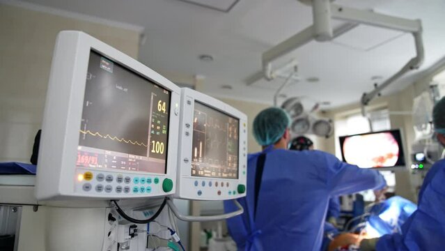 Doubled screen of a lung ventilator working in the surgery room. Medical team working in the backdrop in blur.