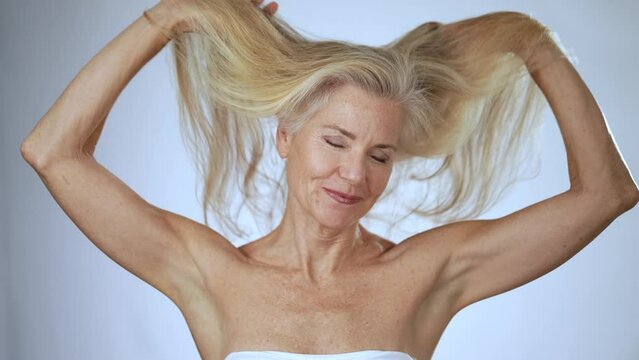Portrait of smiling happy mature, senior, fit woman happy putting fingers through long hair outstretched arms celebrating great freedom hair flying isolated on white background in slow motion.
