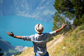 Young man on an alpine hike in the Swiss mountains. He enjoys the beautiful landscape with wide open arms. Alpin mountain panorama