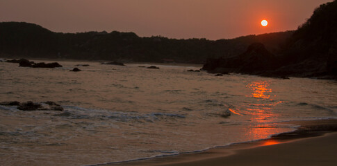 Playa y mar con Sol de fondo metiéndose entre las montañas durante el atardecer en Oaxaca