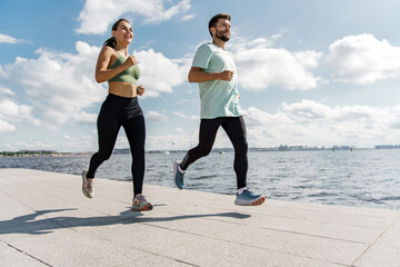 A young family is engaged in sports for health. A woman and a man running around in sports clothes. A group of friends use running shoes. Coach and client. Together athletes workout fitness.