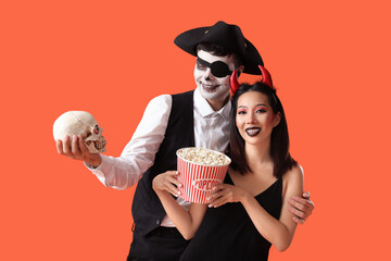 Young couple dressed for Halloween with popcorn and skull on red background