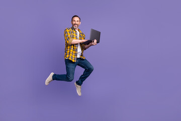 Photo of funky cheerful guy wear plaid clothes hand hold use macbook run empty space buy modern device isolated on purple color background