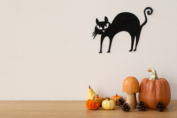 Halloween pumpkins with mushroom and fir cones on table near light wall