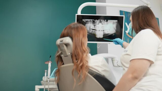 In the dental office, the patient examines detailed images of her dentition. The dentist conducts a detailed analysis and explains the condition of the teeth on X-rays and panoramas of tomography
