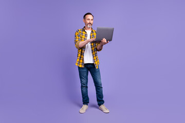 Full body photo of good mood clever person dressed checkered shirt jeans look at laptop read email isolated on violet color background