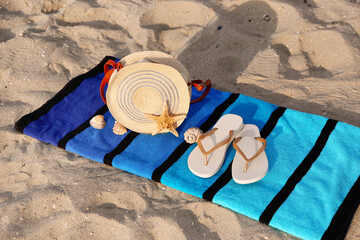 Towel with stylish female bag, flip-flops and seashells on sand