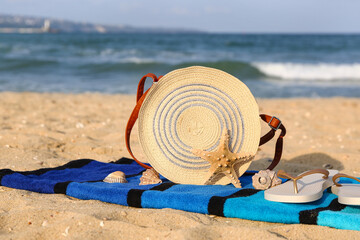 Fototapeta na wymiar Towel with stylish female bag, flip-flops and seashells on sand