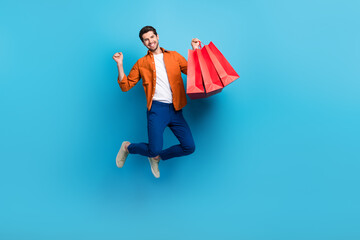 Full length photo of excited delighted man jumping hand hold boutique mall bags raise fist isolated...