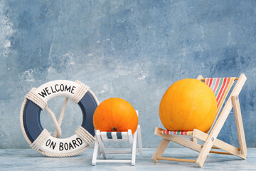 Halloween pumpkins with beach deck chairs and lifebuoy ring on blue background