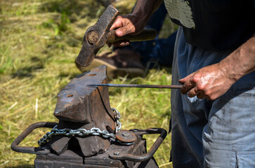 The blacksmith manually with hammer working with metal on the anvil in the open air