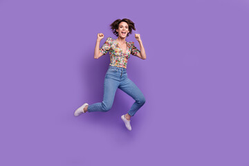 Full size photo of delighted overjoyed girl jumping raise fists empty space ad isolated on violet color background