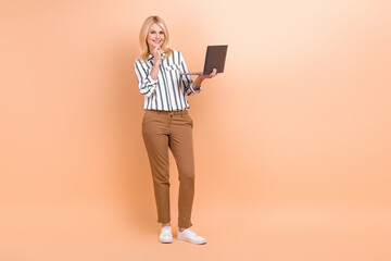 Full length photo of cute clever woman dressed striped shirt typing emails modern device empty space isolated beige color background