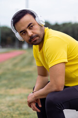 portrait of tired Sports man wears wireless headphones sits after a workout at the sports arena.