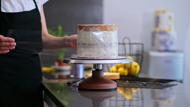 Focused confectioner showing process wrapping process of making creamy homemade woman in apron putting white mastic on baked dough with pastry cone