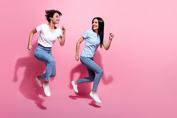 Full body photo of two young sisters family relationship running jump hurry buy last coupon final sale isolated on pink color background