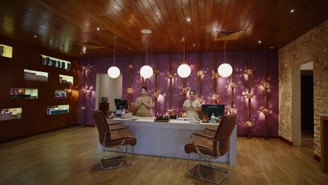 Asian spa staff greeting in reception hall. Hotel lobby receptionists say hello. Luxury wellness center workers greet with Anjali Mudra namaste pose. Thai masseuse smile at camera in beauty clinic