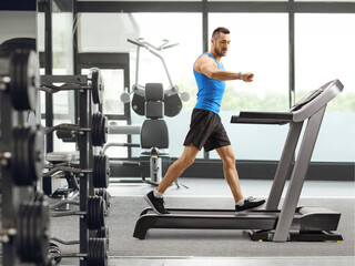 Fototapeta premium Guy exercising on a treadmill and looking at his smartwatch inside a gym