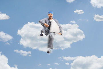 Man in pajamas with a sleeping mask holding a pillow and sitting on a cloud