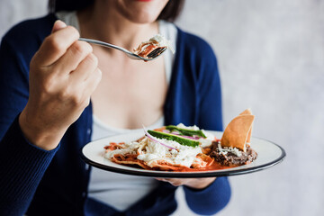 Mexican woman eating chilaquiles with red sauce, cooking traditional mexican food for breakfast in Mexico Latin America, hispanic people