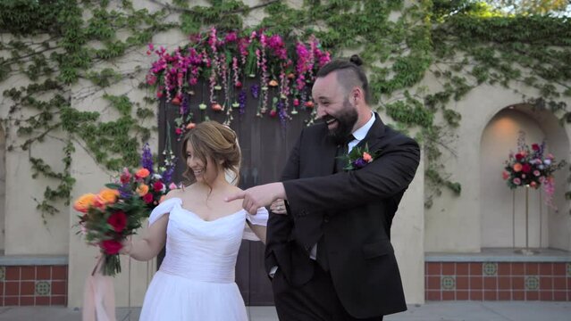 Smiling wedding couple walking forward, pointing fingers at sides, laughing. Bride and groom coming to the rows of seats, standing outdoors. Wedding venue. High quality 4k footage