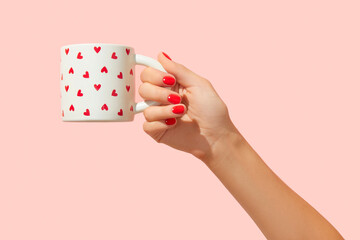 Womans hand with red manicure holding cup on pink background. Minimalist nail design