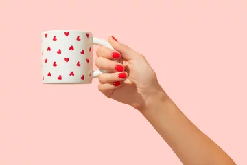  Womans hand with red manicure holding cup on pink background. Minimalist nail design © Darya Lavinskaya