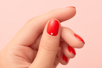 Close up womans hand with red minimalist nail design on pink background