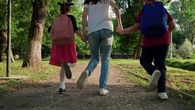 Happy family mom daughter son holding hands run rush to school on path. School children with their mother run to school. Boy girl mom walking outdoors. Kids with backpacks runs in park. Concept family