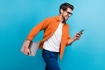 Fototapeta premium Profile photo of handsome manager man walking hold netbook use smart phone texting isolated on blue color background