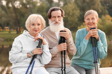 Group of senior people with Nordic walking poles sitting on wooden parapet outdoors