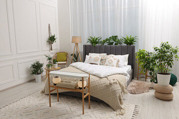 Large comfortable bed, lamp and beautiful houseplants in bedroom. Interior design