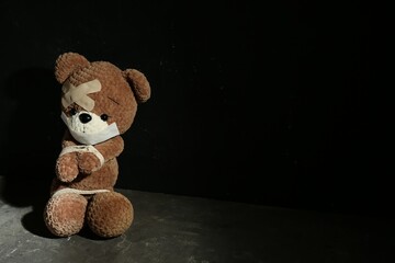 Stop child abuse. Tied toy bear with taped mouth and patches on grey floor against black background. Space for text
