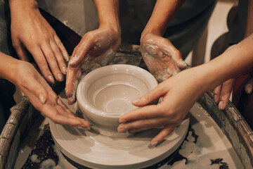 three women are working on a potter's wheel, making a vase.