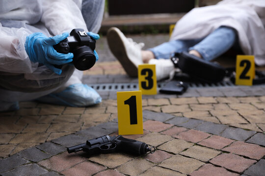Criminologist taking photo of evidence at crime scene with dead body outdoors, closeup. Space for text