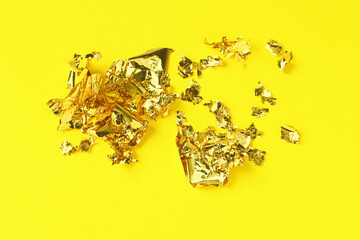 Many pieces of edible gold leaf on yellow background, top view