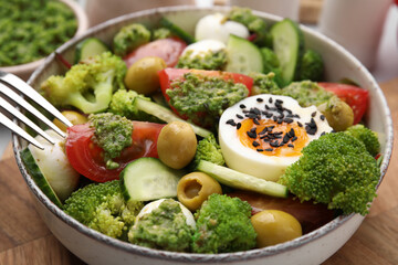 Delicious salad with pesto sauce in bowl and fork on table, closeup
