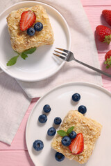 Pieces of delicious Napoleon cake with fresh berries served on pink wooden table, flat lay