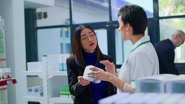 Shopper in modern chemist store asking helpful pharmacist for medical expertise. Licensed druggist helping customer trying to pick best pharmaceutical product to fight fever