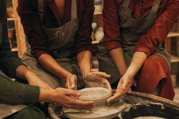 three women are working on a potter's wheel, making a vase.