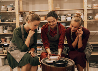 A company of three pretty young women friends make ceramic mugs in a pottery workshop.