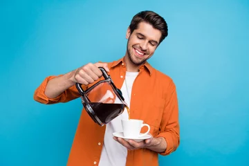 Zelfklevend Fotobehang Photo of cute positive guy wear orange shirt pouring coffee cup isolated blue color background © deagreez