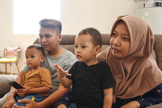 Happy Asian muslim family watching TV together at living room in modern house.