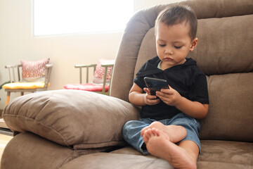 Adorable Asian boy sitting on the sofa in the living room and playing with smartphone. 