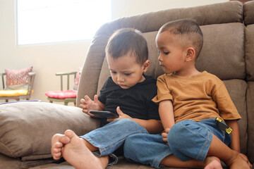 Two happy toddler boy watching video on smartphone together at home. 