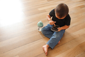 Little Asian boy child sitting on floor using smartphone at home, playing mobile game on cell phone. 