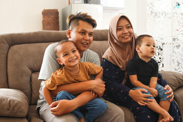 Happy Asian muslim family sitting and watching television in living room at home and spent quality time together. Happiness, parenting or lifestyle concept.
