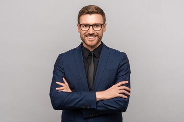 Portrait of happy successful confident businessman in suit with crossed arms on chest smiling looking at camera on grey background. Man entrepreneur in eyeglasses on advertisement poster, banner. - obrazy, fototapety, plakaty