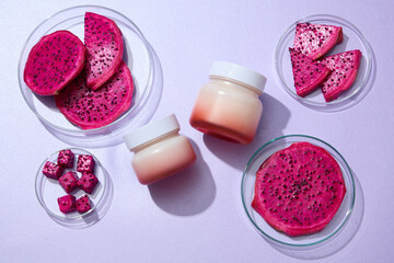 Two cream jars decorated with some petri dishes containing red dragon fruit slices on a purple background. Top view, mockup jars unlabeled for design. Concept for advertising natural cosmetics
