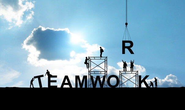Silhouette of construction workers as a team working together to put letters as a word teamwork on a bright sky background